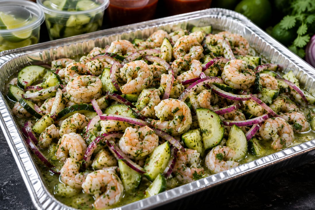 Seafood Party Trays — Large foil catering tray of shrimp aguachile with cucumber and red onion, with cucumber and salsa side cups